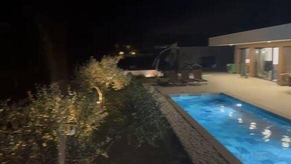 Beleuchteter Swimmingpool und Außenbereich bei Nacht, umgeben von Bäumen.