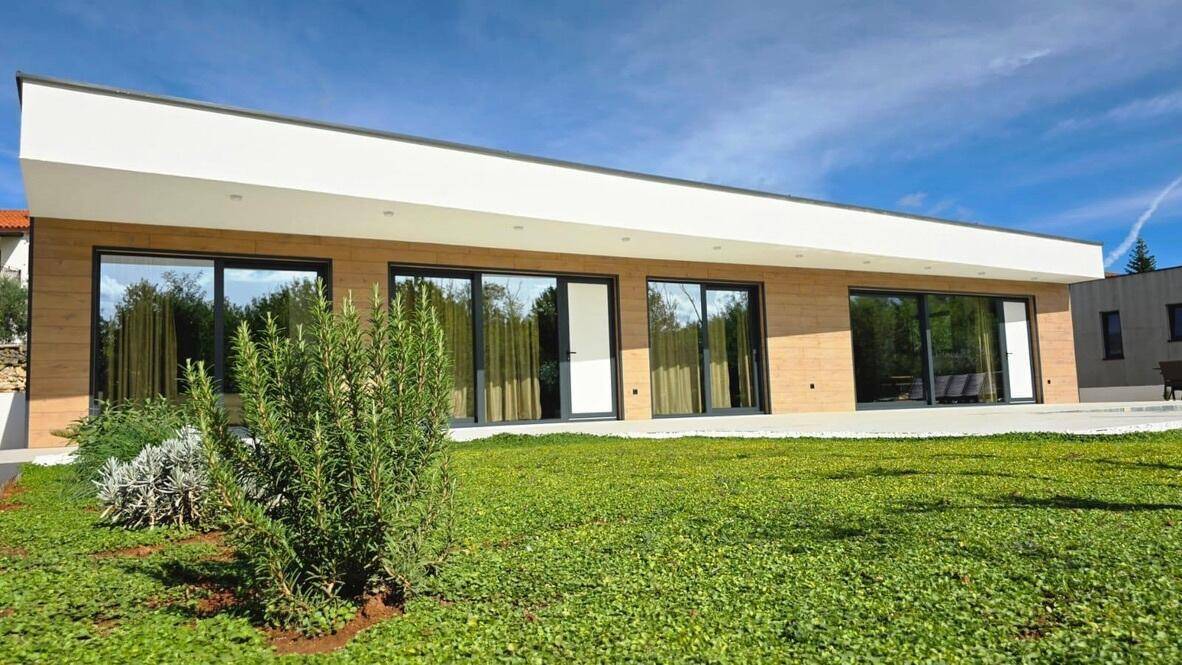 Moderne Hausfassade mit Holzverkleidung, großen Fenstern und gepflegtem Rasen.