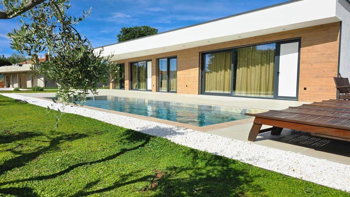 Moderner Außenbereich mit Swimmingpool, Liegestühlen und gepflegtem Rasen unter blauem Himmel.