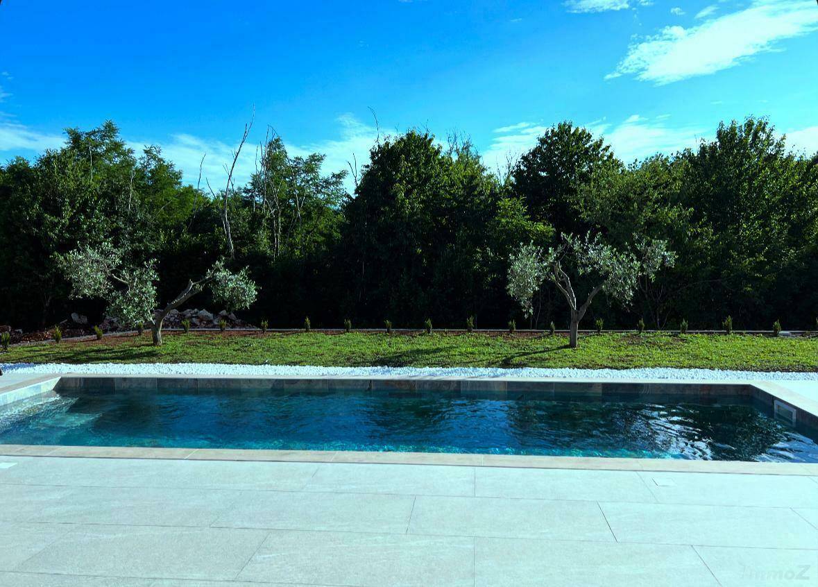 Klarer Swimmingpool mit weißem Kiesrand und Blick auf die umliegende Natur.