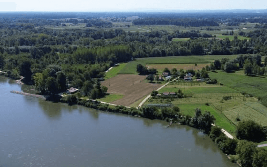 Luftaufnahme einer Flusslandschaft mit Feldern, Waldgebieten und kleinen Siedlungen am Ufer.