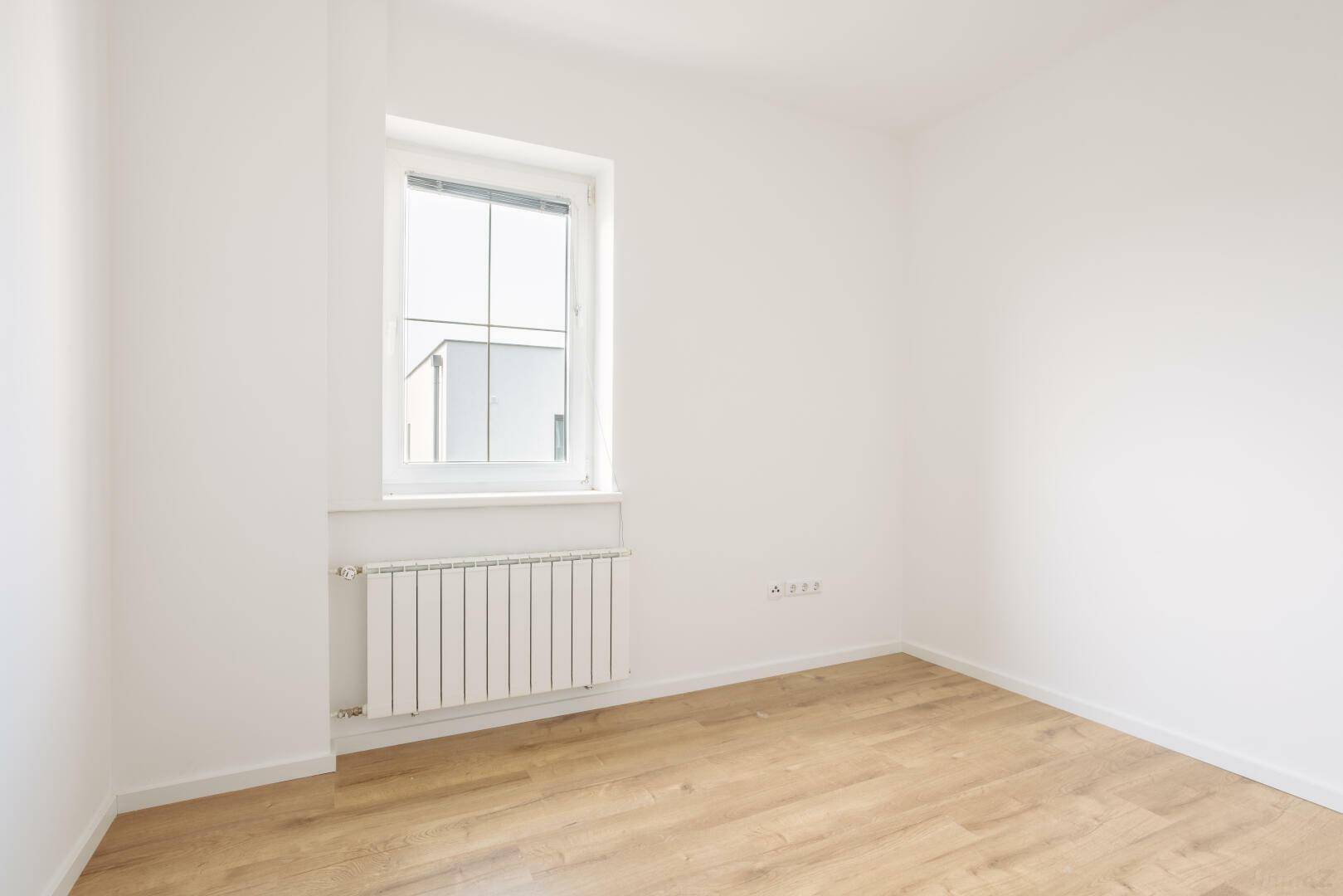 Helles Zimmer mit Laminatboden und großem Fenster, ideal als Schlaf- oder Arbeitszimmer.