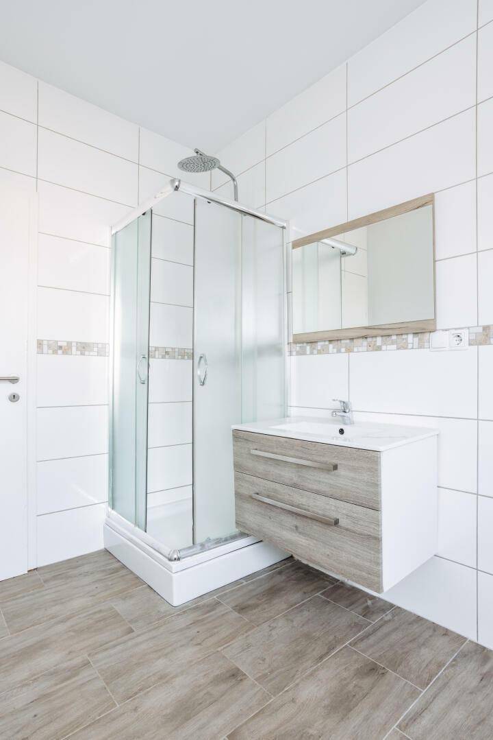 Modernes Badezimmer mit Duschkabine, Waschtisch und hellen Fliesen.