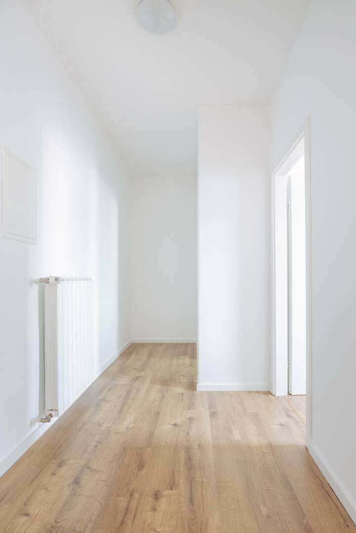 Langer, heller Flur mit Laminatboden und Heizkörper an der Wand.