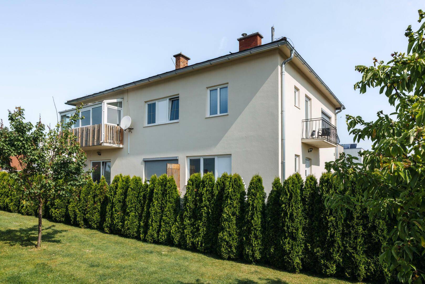 Seitenansicht eines Wohnhauses mit Balkon, verglaster Loggia und gepflegtem Gartenbereich.