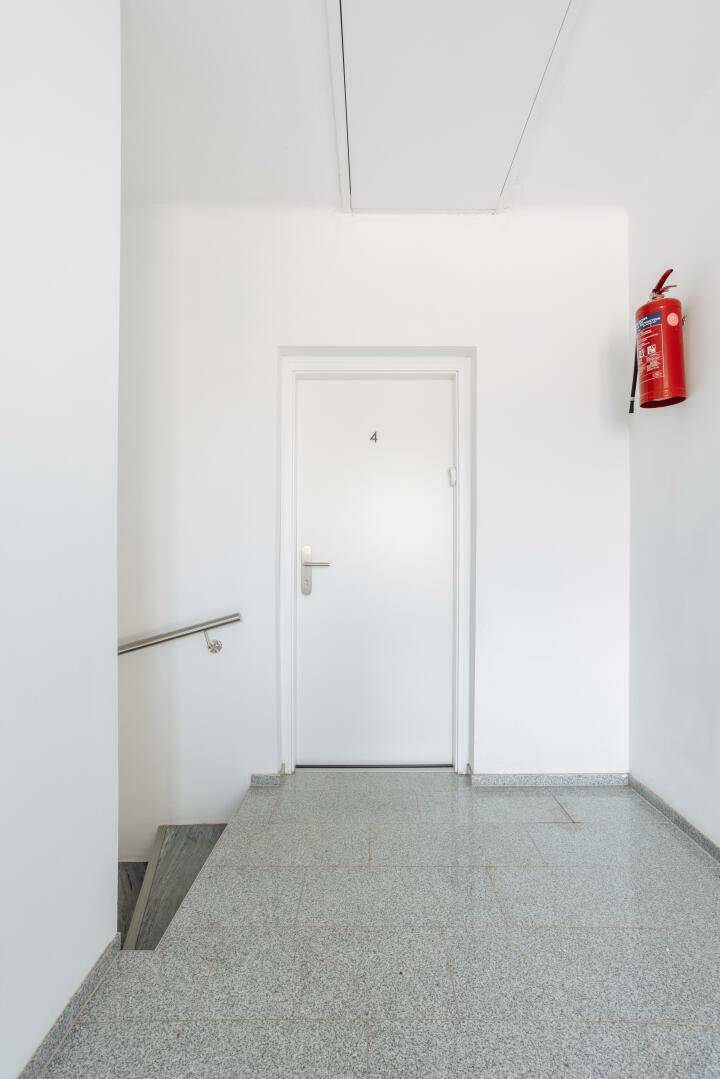 Heller Hausflur mit Terrazzoboden, weißer Tür und Treppenaufgang zu den Wohnungen.
