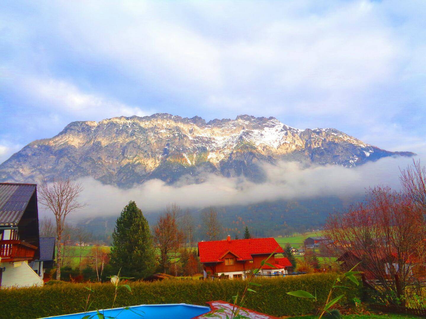 Atemberaubender Blick auf eine majestätische Bergkette mit Wolken und einem Außenpool im Vordergrund.