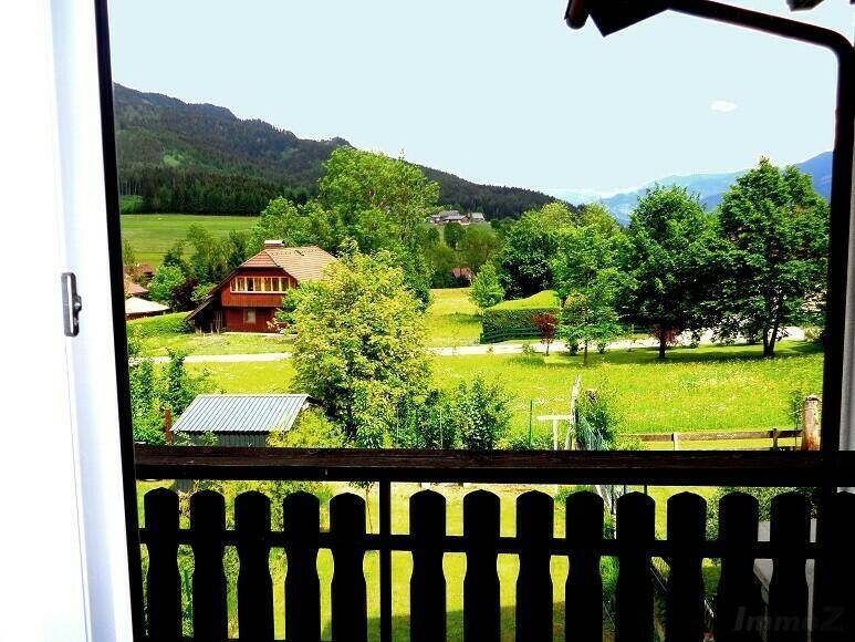 Blick vom Balkon auf die grüne Landschaft mit weiteren Häusern und bewaldeten Bergen.