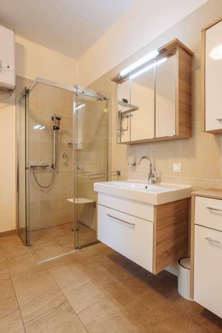 Modernes Badezimmer mit ebenerdiger Dusche, Waschtischunterschrank und hellen Fliesen an Wänden und Boden.
