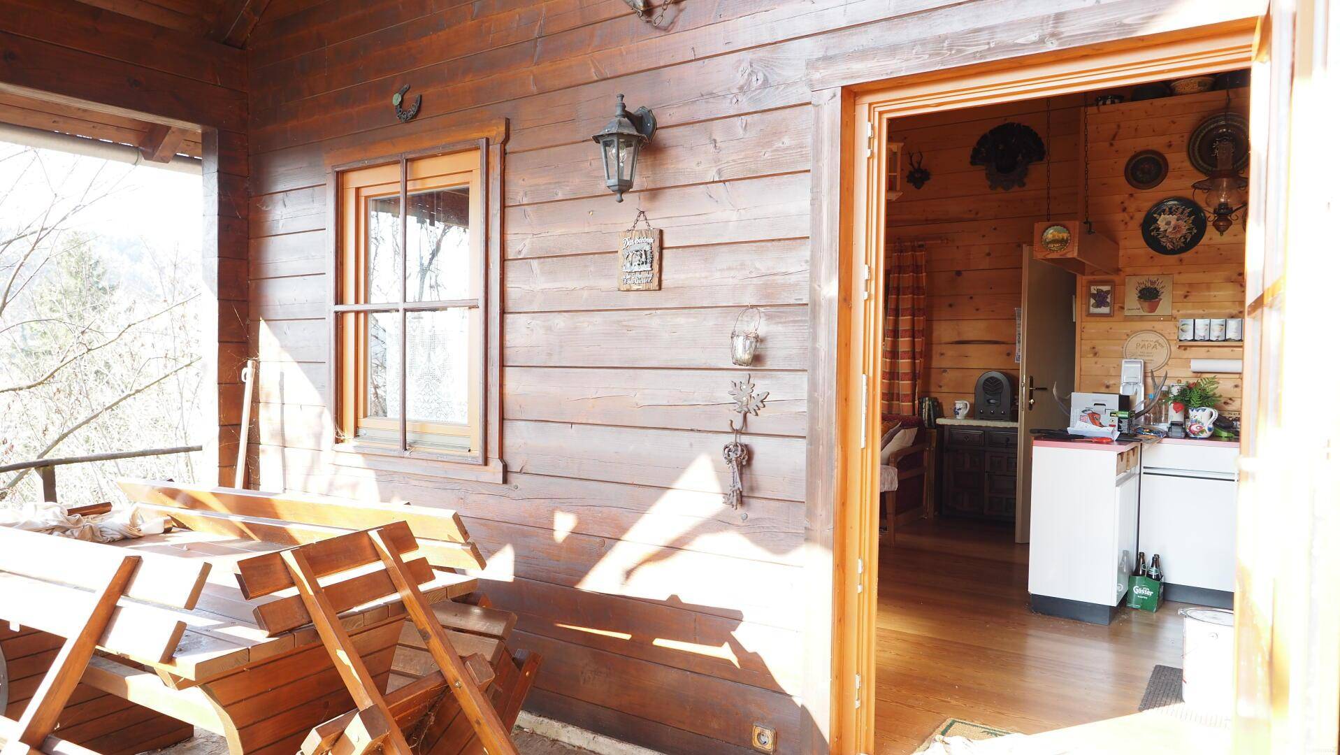 Gemütlicher Holzbalkon mit Sitzgelegenheiten und Blick ins Grüne, angrenzend an eine kleine Küche.