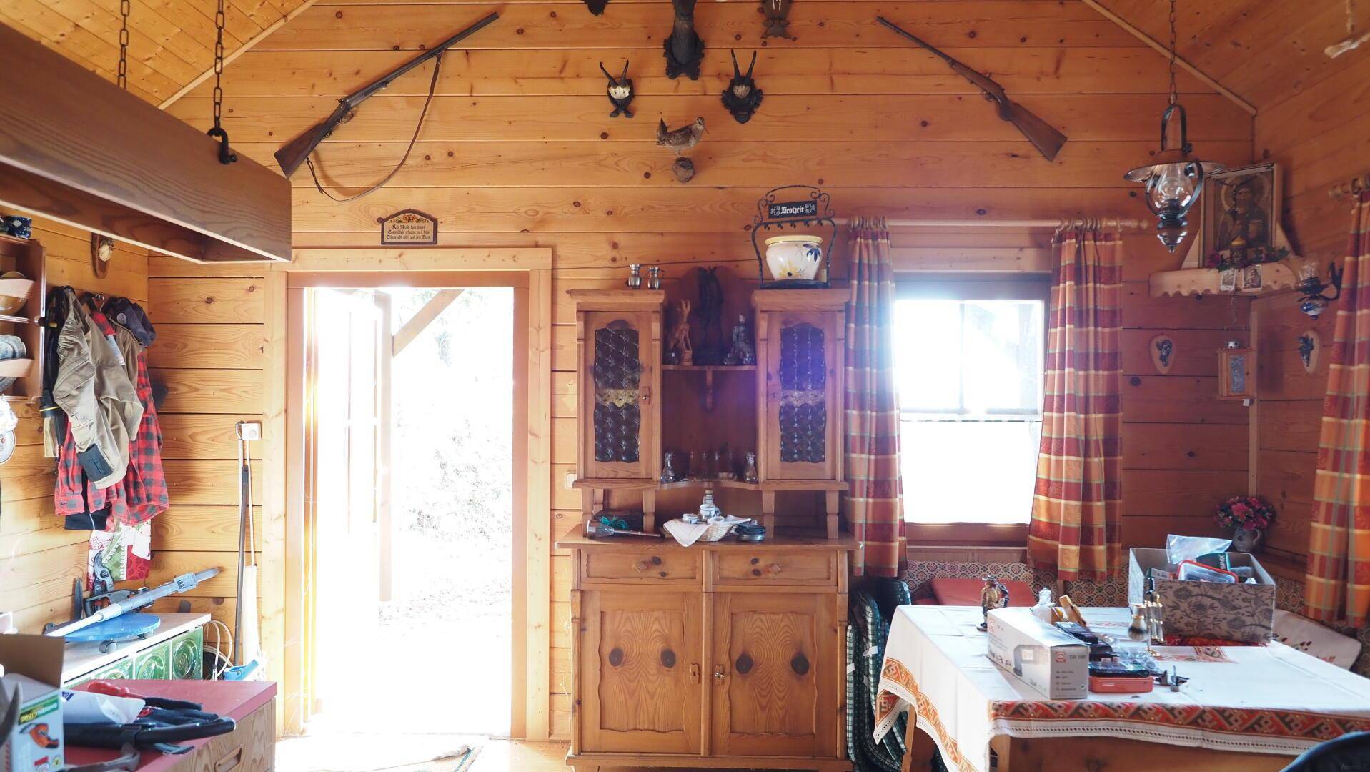 Rustikaler Wohn-Essbereich mit Holzwänden, traditioneller Dekoration und viel Tageslicht durch die Fenster.