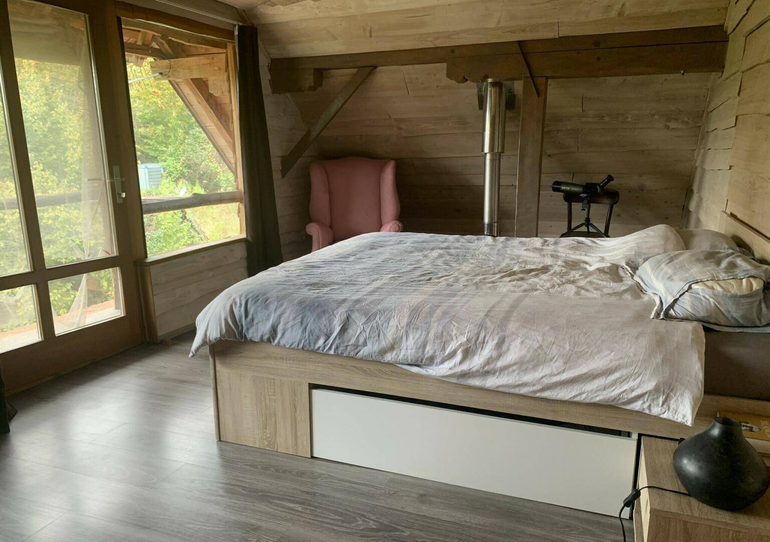 Helles Schlafzimmer mit großem Fenster, Holzbalken und einem Bett mit Stauraum.