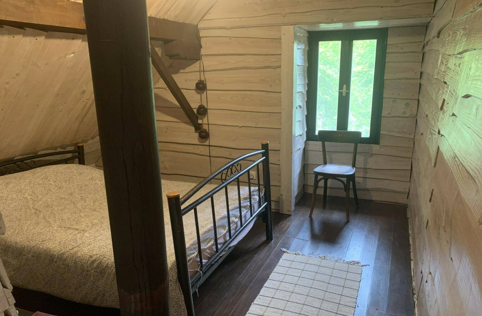 Gemütliches Schlafzimmer mit Holzwänden, einem Metallbett und einem Fenster mit Blick ins Grüne.