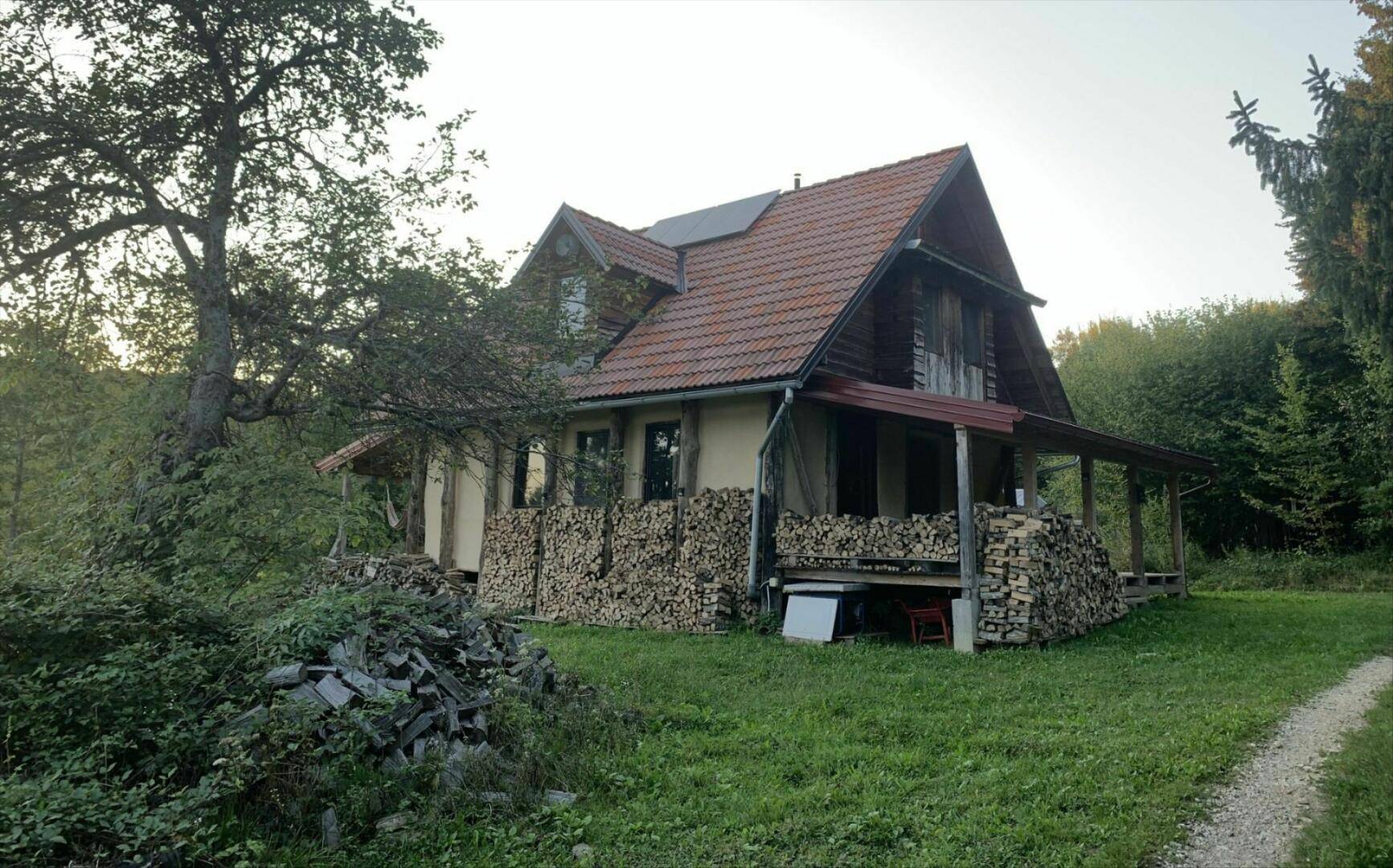 Charmantes Landhaus mit Holzfassade und großen Holzstapeln, umgeben von üppiger Natur.
