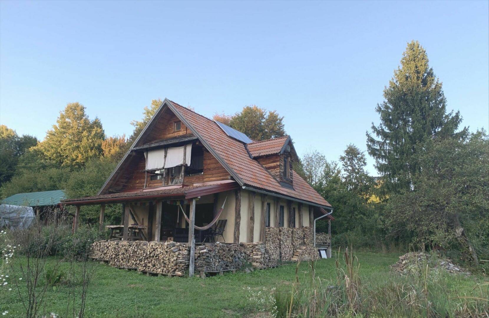 Rustikales Holzhaus mit Ziegeldach, umgeben von Bäumen und einem Holzstapel.
