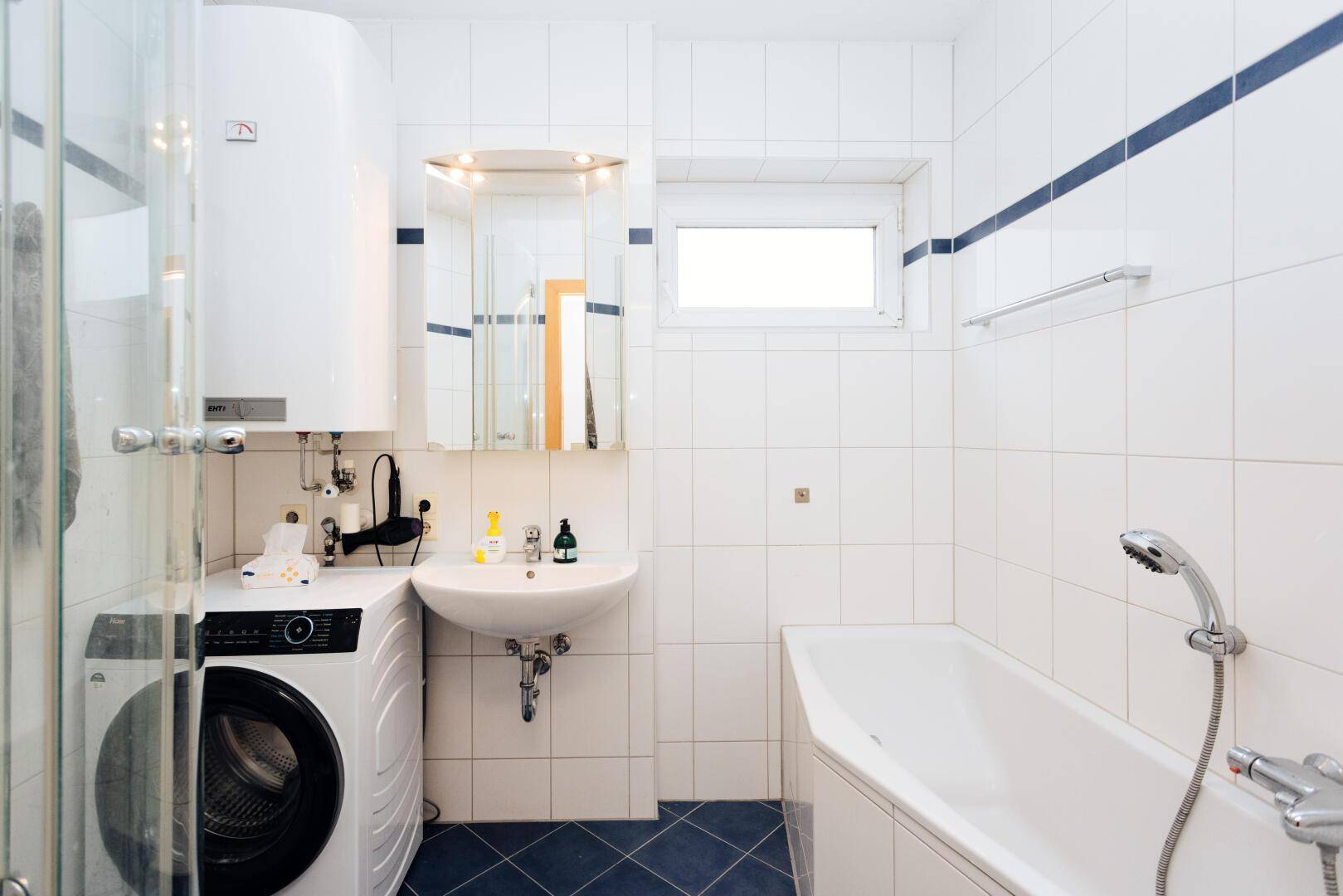 Gefliestes Badezimmer mit Badewanne, Duschbereich, Waschbecken und einer Waschmaschine.