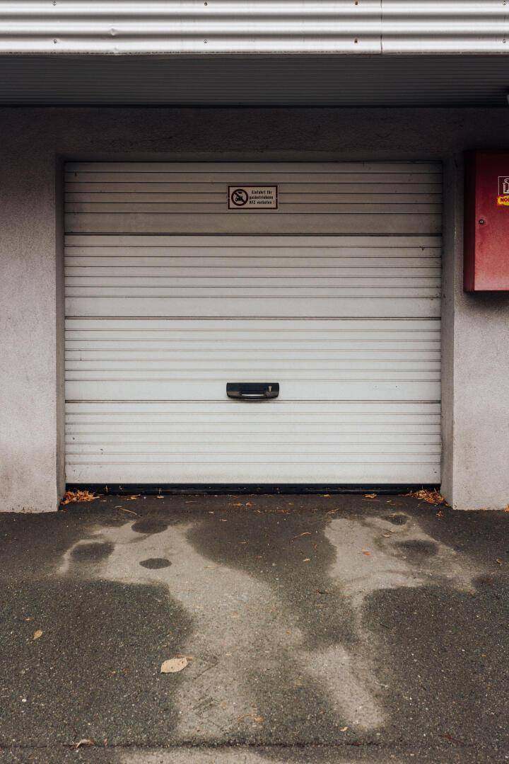 Weiße Garagentür mit horizontalen Lamellen und einem Hinweisschild, Teil eines Parkhauses.