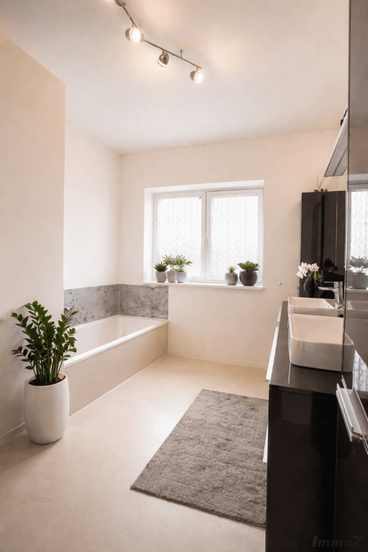 Helles Badezimmer mit Badewanne, Doppelwaschbecken und Fenster für Tageslicht.