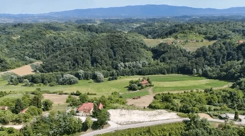 Weitläufige Landschaft mit grünen Hügeln, Wäldern und vereinzelten Häusern.