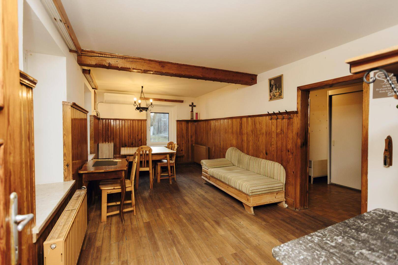 Rustikaler Wohn-Essbereich mit Holztäfelung, sichtbaren Deckenbalken und traditionellen Möbeln.