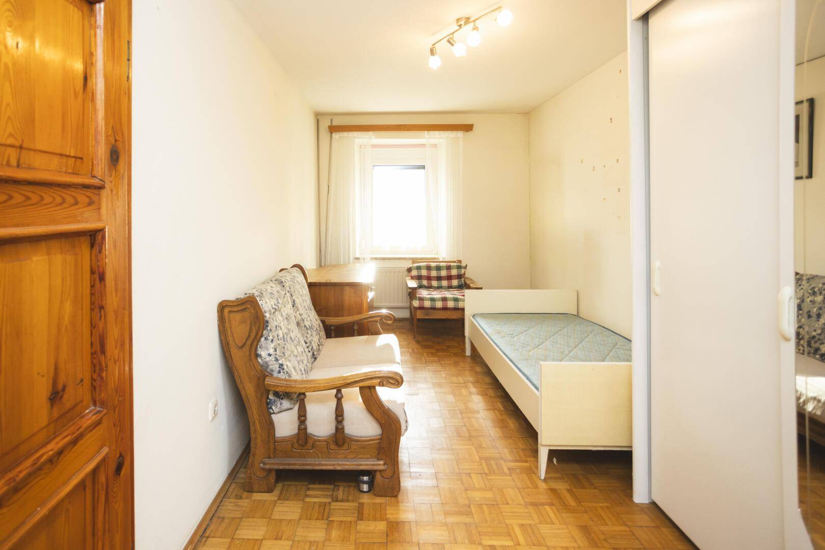 Helles Gästezimmer mit Einzelbett, Holzmöbeln und Parkettboden.