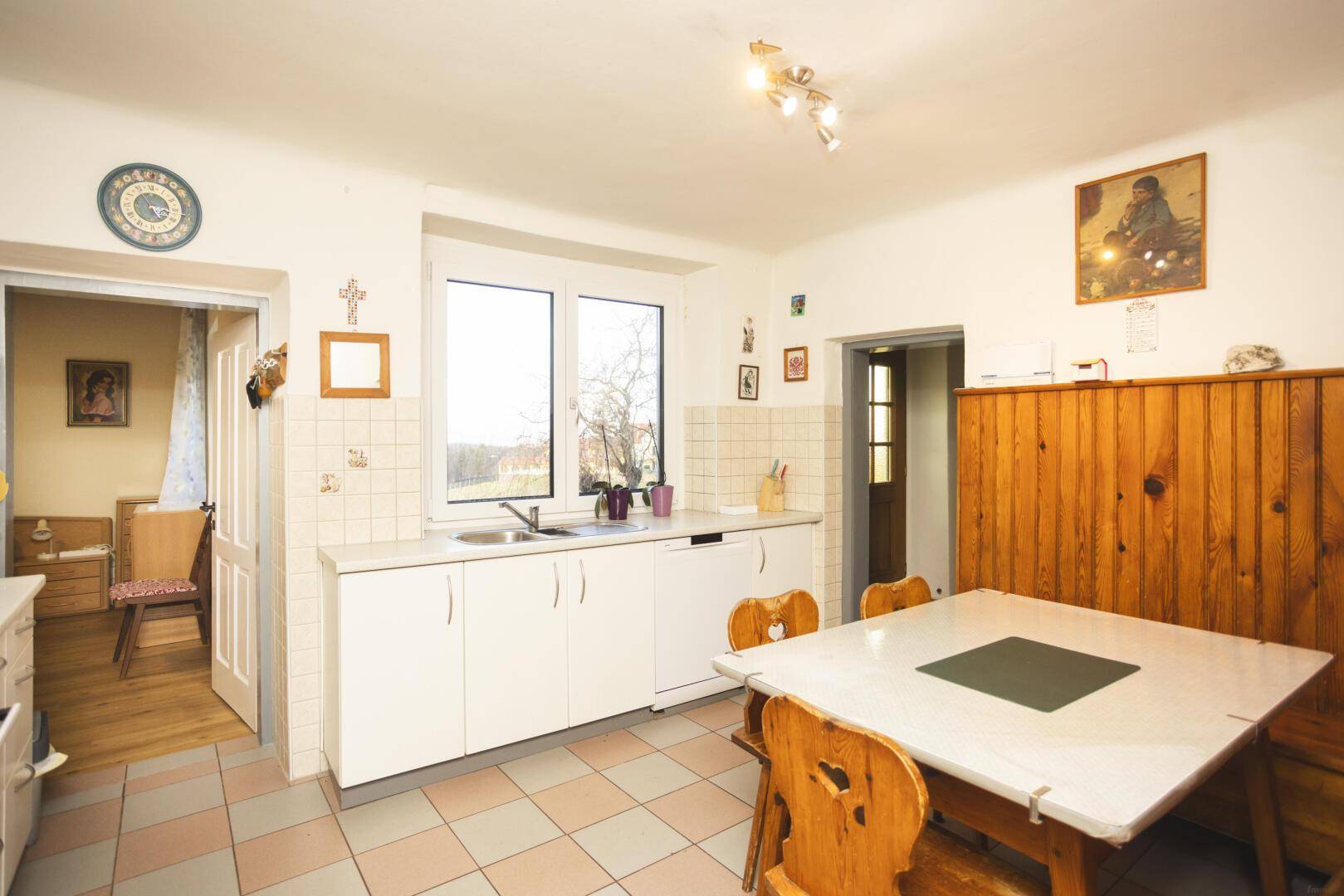 Helle Wohnküche mit weißer Einbauküche, Essbereich und Blick ins Grüne durch das Fenster.