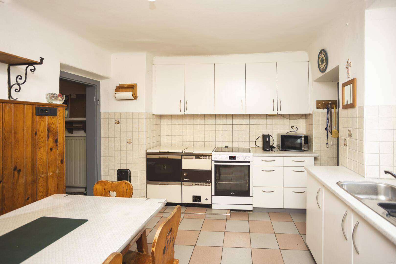 Funktionale Küche mit traditionellem Holzofen, modernem Backofen und weißen Küchenschränken.