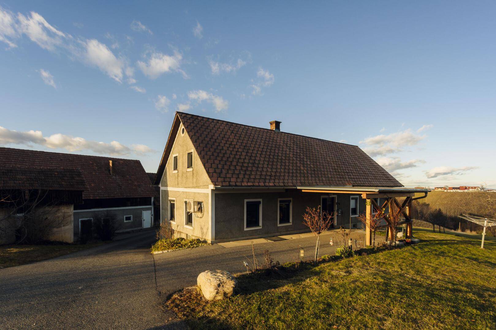 Ländliches Wohnhaus mit überdachtem Eingangsbereich und Satteldach, umgeben von grüner Wiese.