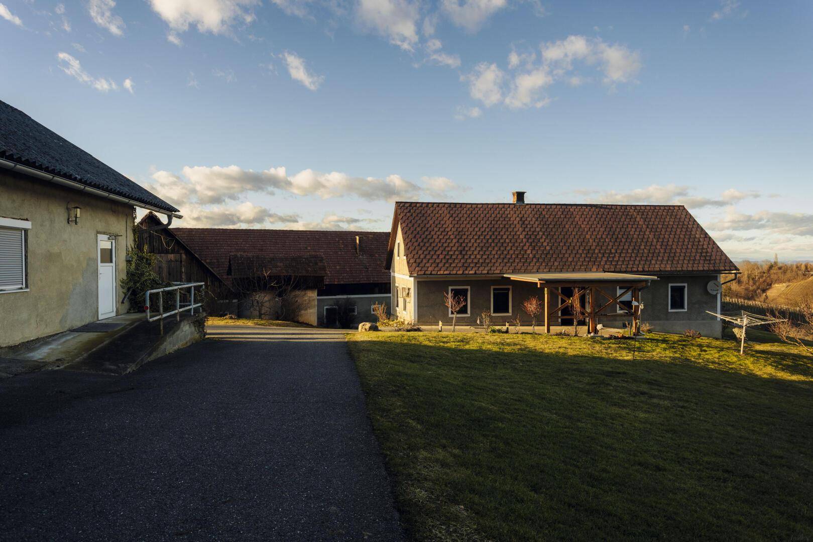 Ansicht des Haupthauses mit Satteldach und einem weiteren Gebäude im Hintergrund, umgeben von Wiese.