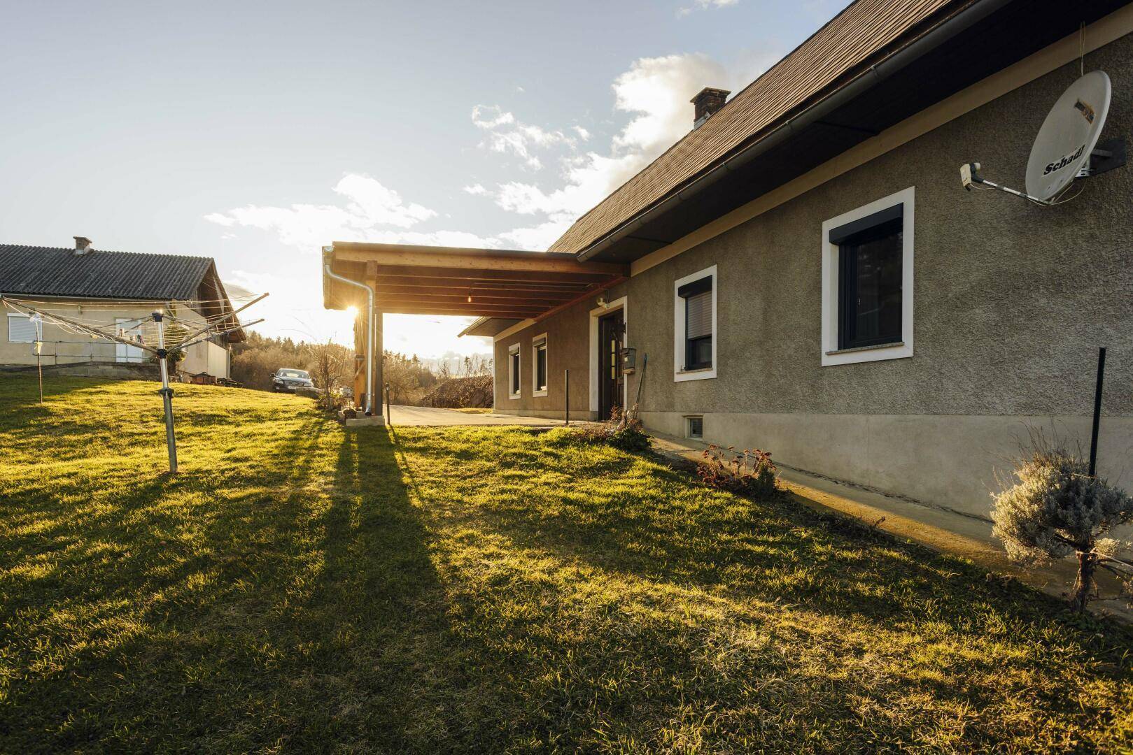 Seitenansicht des Wohnhauses mit überdachtem Bereich und Wäscheleine auf der grünen Wiese.