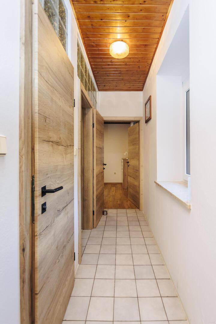 Heller Flur mit modernen Holztüren, Fliesenboden und Holzdecke.