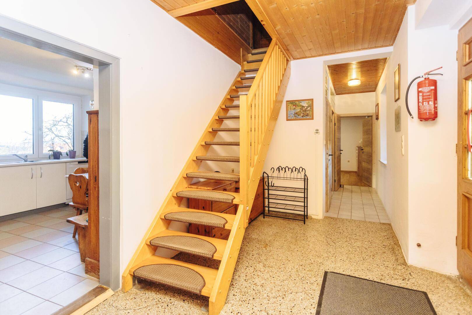 Heller Flur mit Holztreppe, Terrazzoboden und Zugang zu weiteren Räumen.