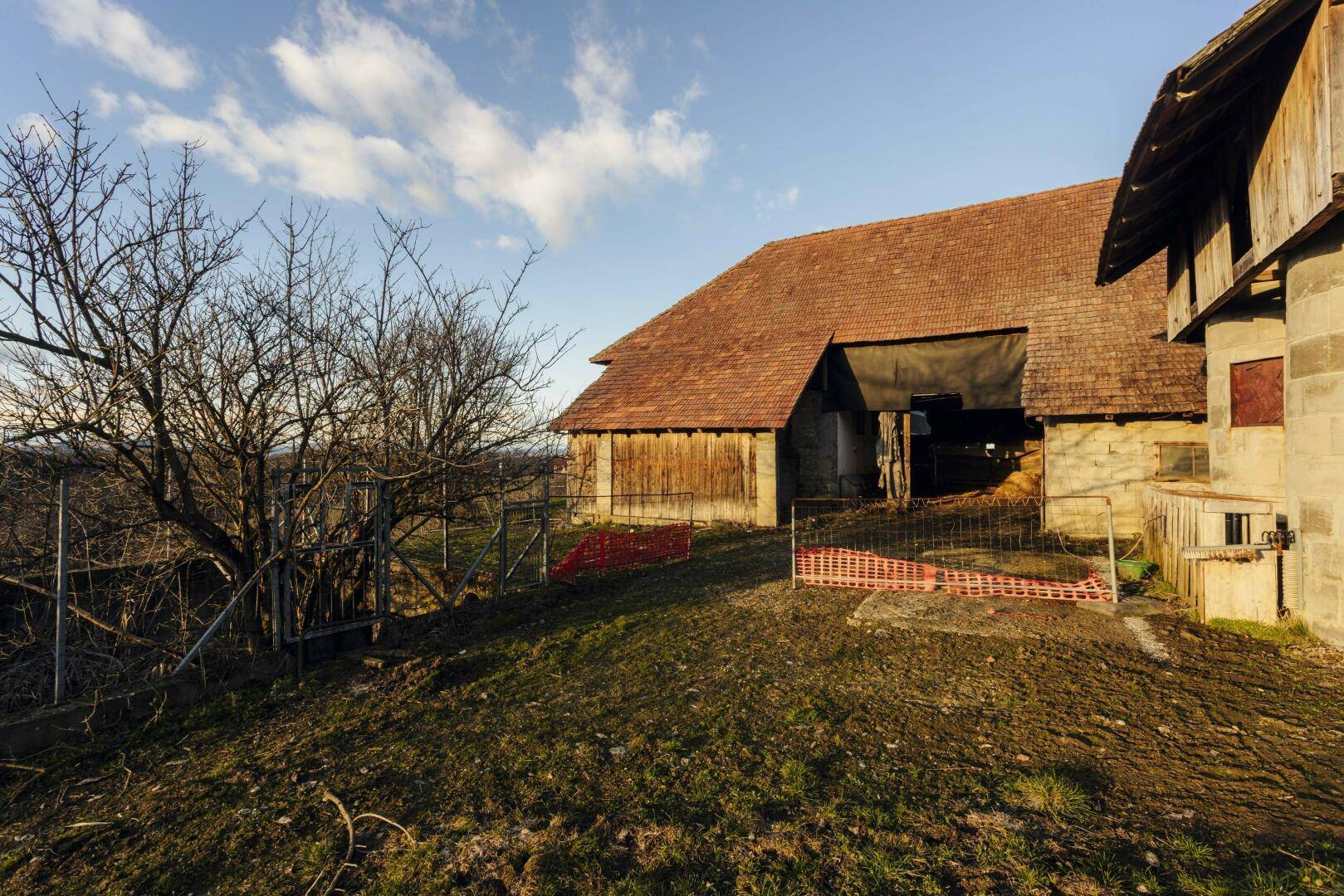 Ländliches Scheunengebäude mit Holzwänden und Ziegeldach, umgeben von Wiese.