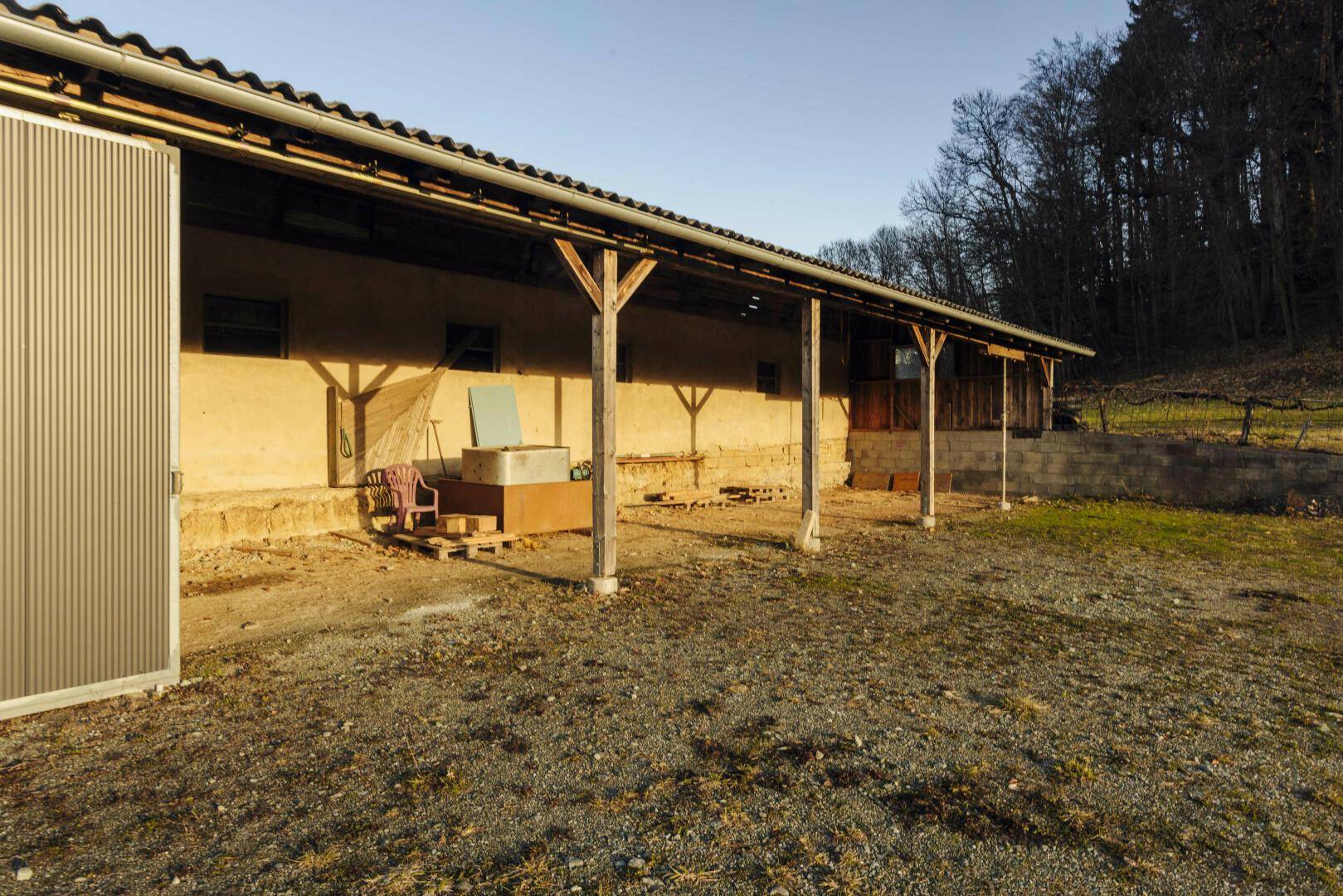 Überdachter Außenbereich mit Holzsäulen und Zugang zu einem landwirtschaftlichen Gebäude.