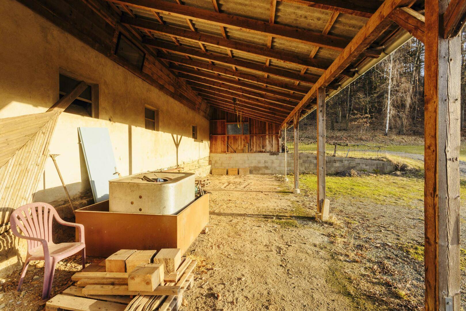 Überdachter Außenbereich neben einem landwirtschaftlichen Gebäude, genutzt als Lagerfläche.