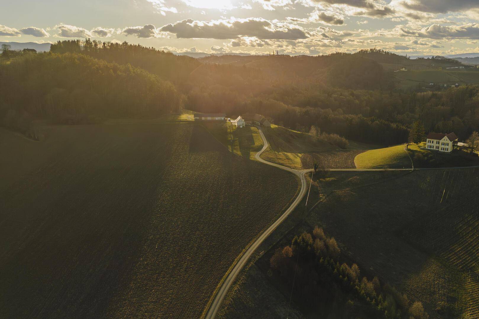 Weitläufige Luftaufnahme der hügeligen Landschaft mit Feldern, Wäldern und vereinzelten Häusern.
