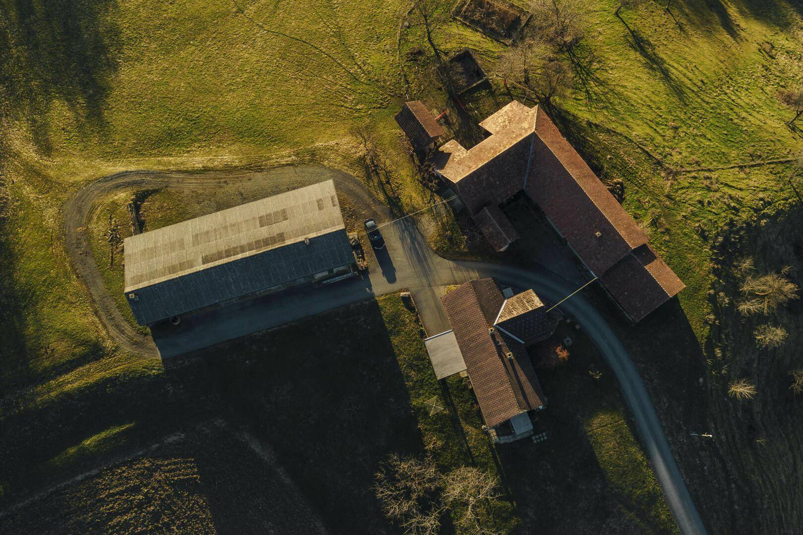 Senkrechte Luftaufnahme des Anwesens mit Gebäuden und umliegenden Feldern in der Abendsonne.