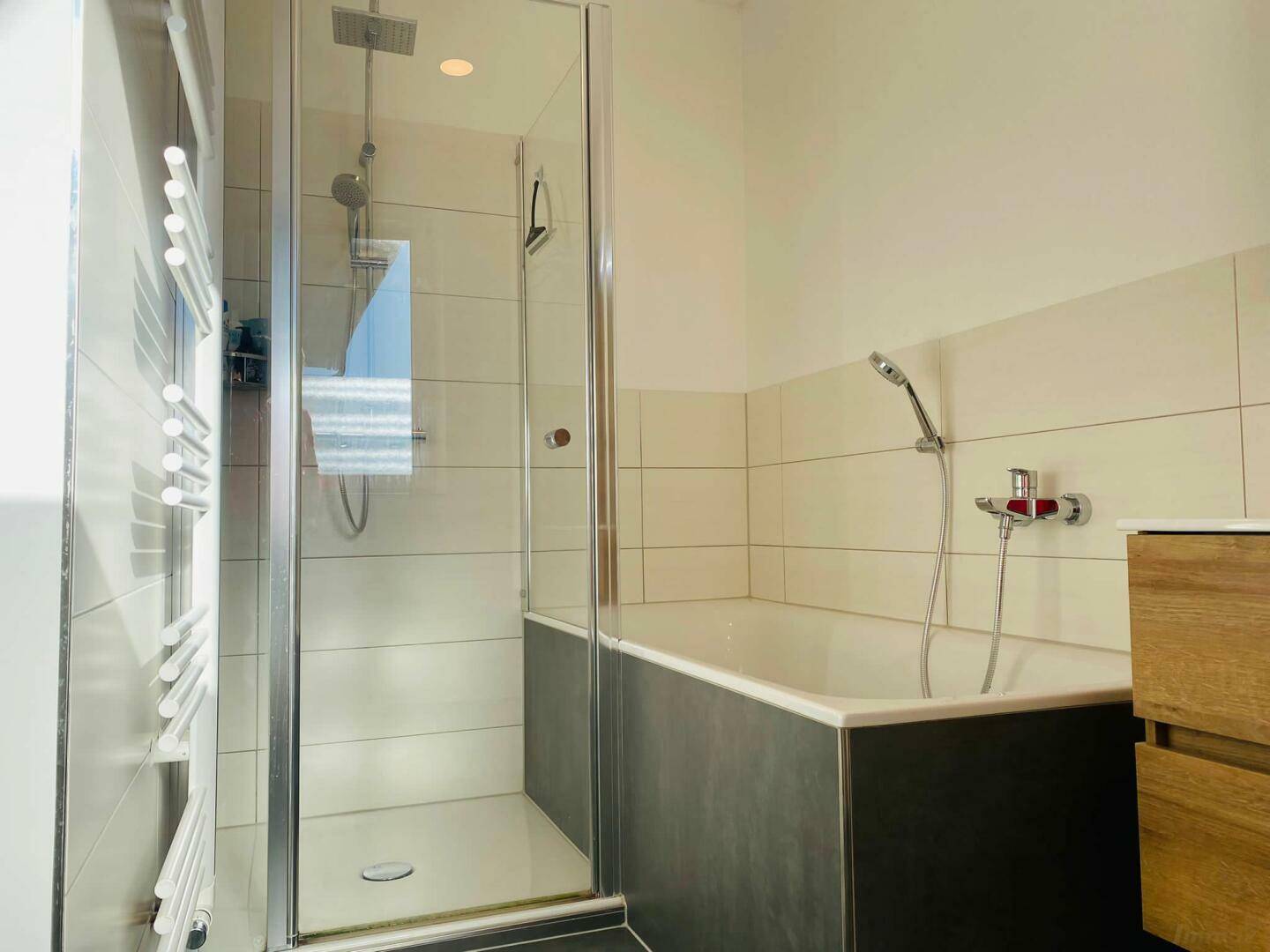 Helles Badezimmer mit Badewanne, Duschkabine und beheiztem Handtuchhalter.