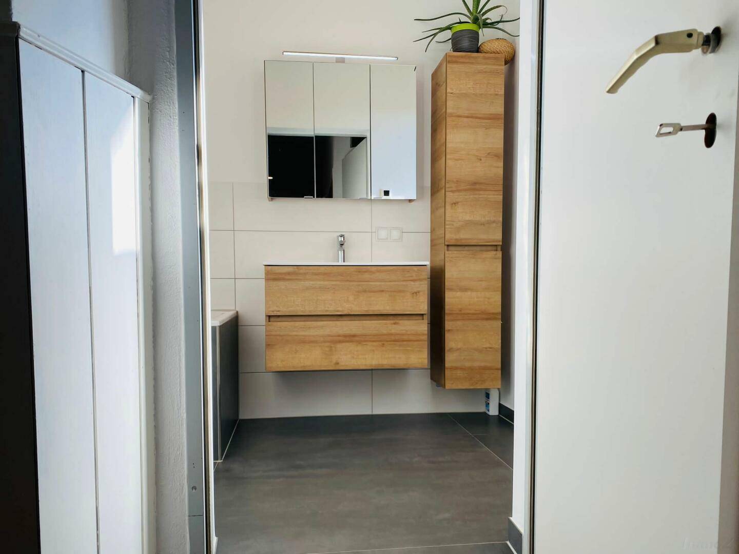 Modernes Badezimmer mit Holzwaschtisch, Spiegelschrank und dunklem Fliesenboden.