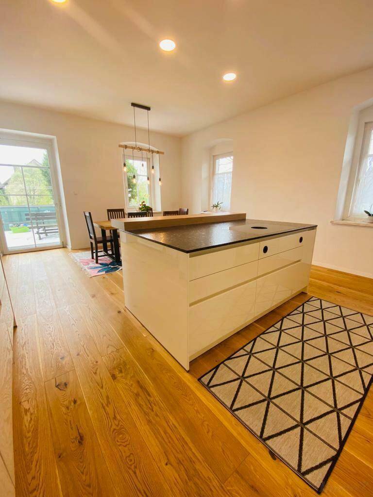 Offener Wohn- und Essbereich mit moderner Kücheninsel und Holzboden, hell und geräumig.