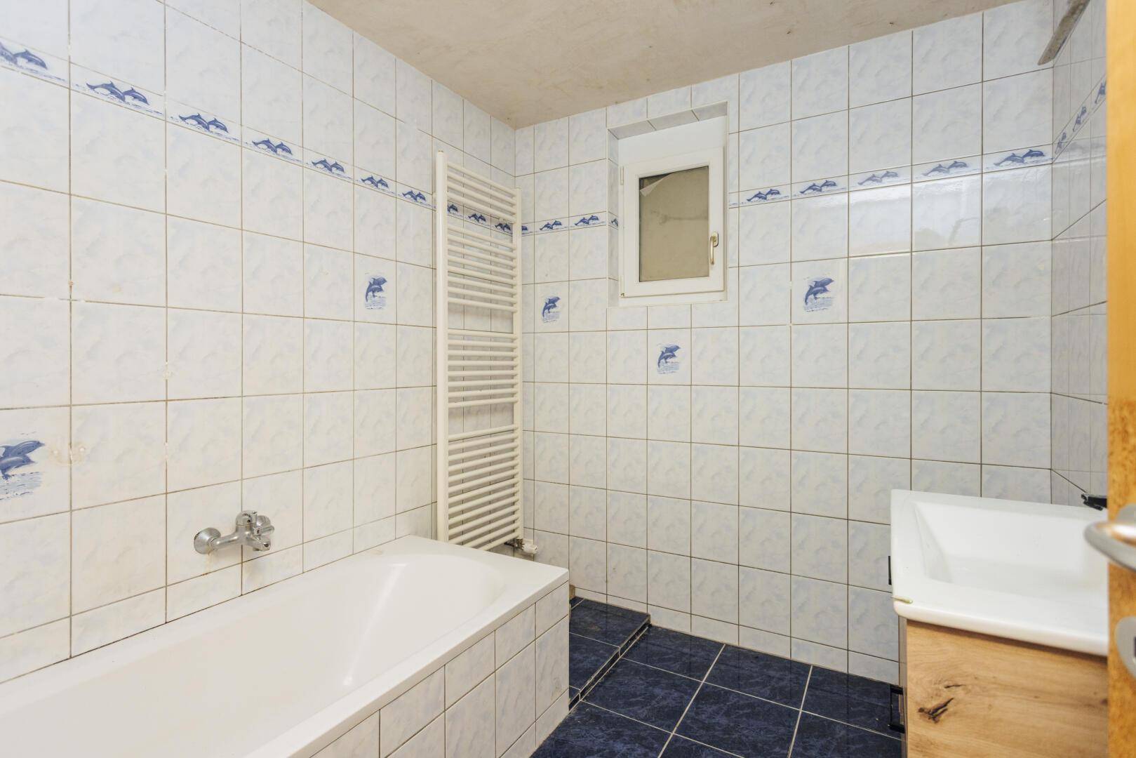 Badezimmer mit blauen und weißen Fliesen, Badewanne und Fenster.