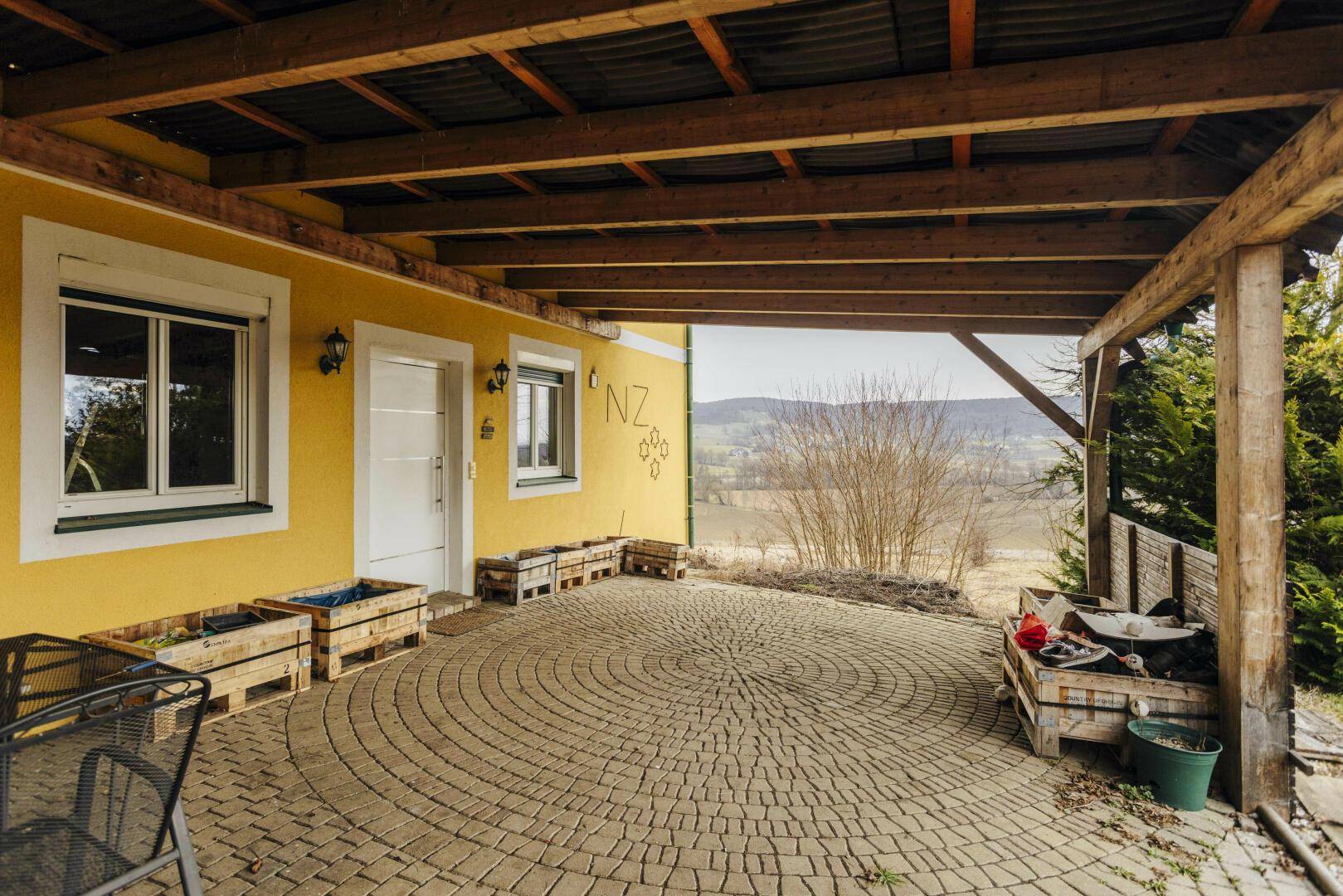 Überdachte Terrasse mit kreisförmigem Pflastermuster und Blick ins Grüne.