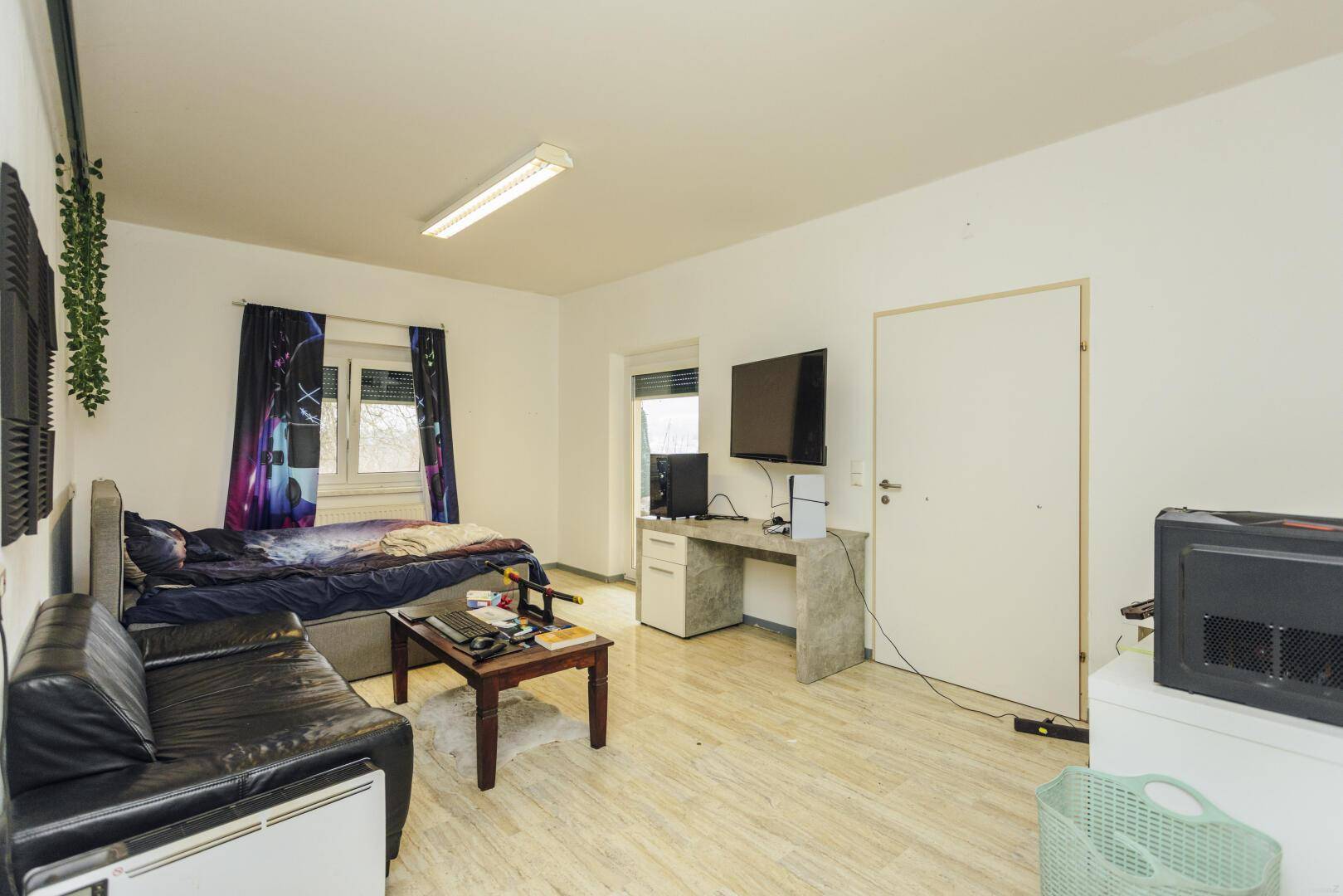 Schlafzimmer mit Bett, Sofa, Schreibtisch und Fenster mit Rollladen.