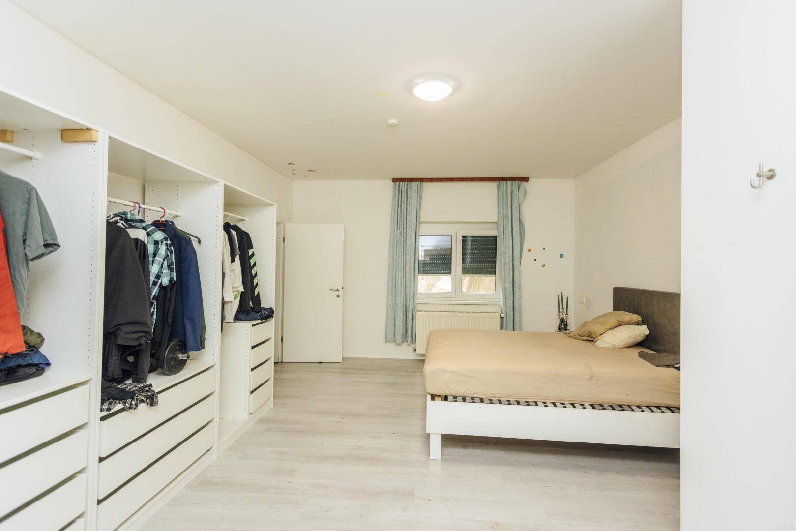 Schlafzimmer mit Doppelbett und offenen Kleiderschränken entlang einer Wand.