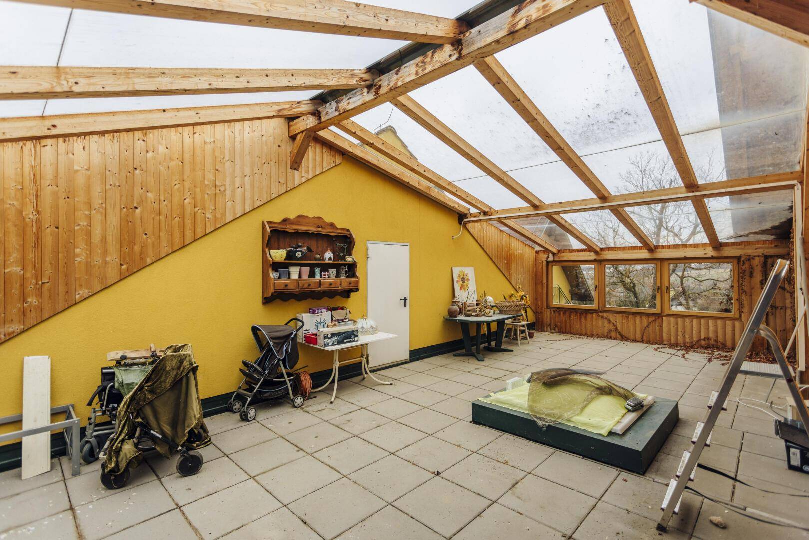 Geräumiger Wintergarten mit viel Tageslicht, Holzverkleidung und Fliesenboden.