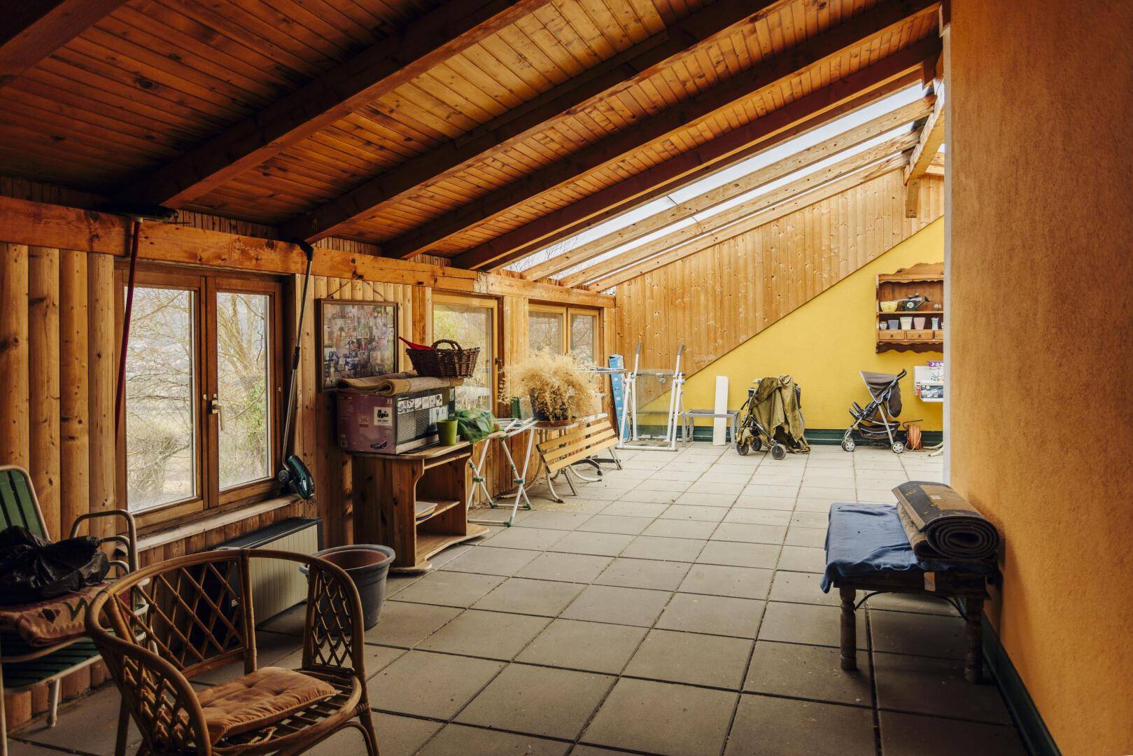 Heller Wintergarten mit Holzdecke, Fliesenboden und großen Fenstern.