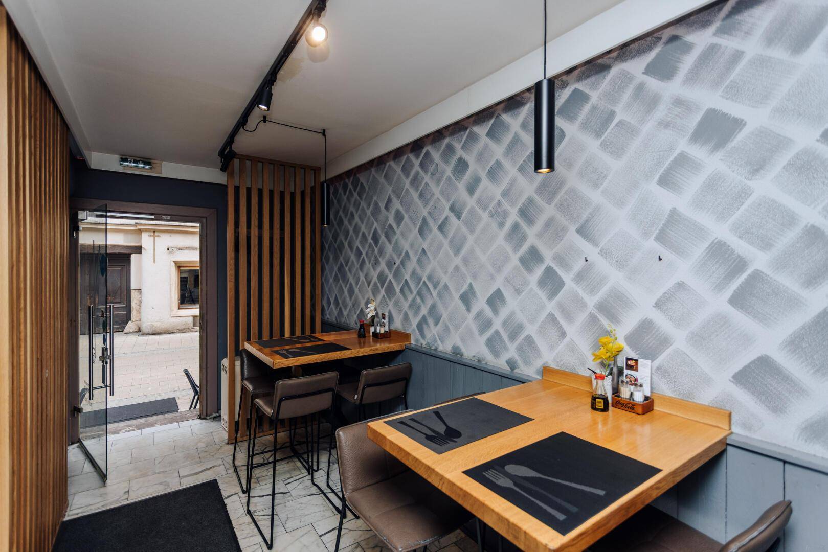 Moderner Restaurantbereich mit Holztischen, Barhockern und einer Holztrennwand am Eingang, die Privatsphäre bietet.