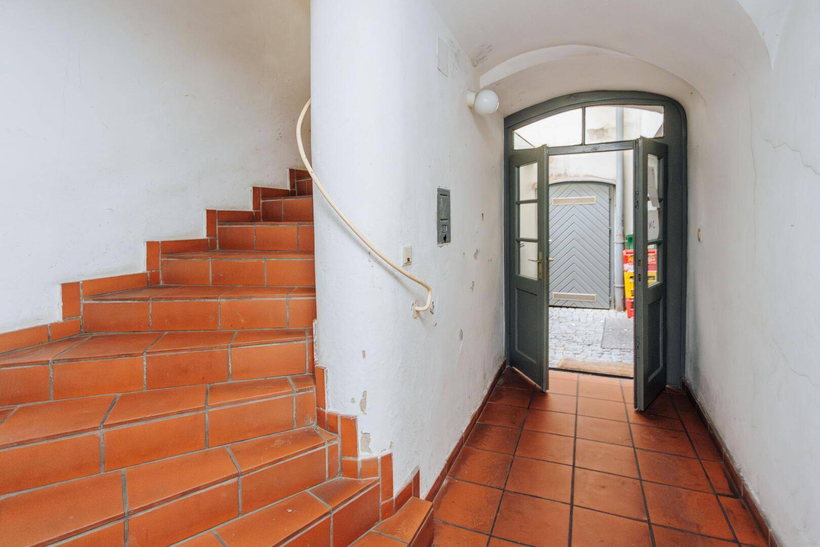 Historisches Treppenhaus mit Terrakottafliesen und einem offenen Ausgang zu einem gepflasterten Hof.