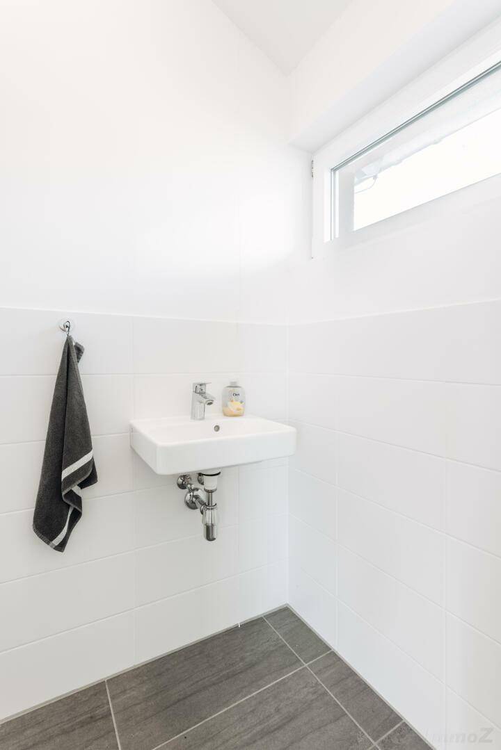 Helles Gäste-WC mit kleinem Waschbecken, Fenster und weißen Wandfliesen.