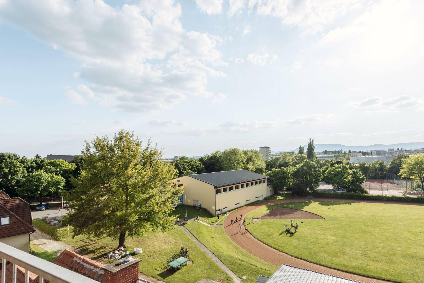 Panoramablick von der Terrasse auf eine weitläufige Grünfläche und die Stadt.